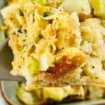 A close-up of a serving of Sourdough Stuffing with chopped celery and herbs, lifted on a spatula from a casserole dish.