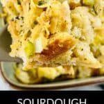 Close-up of a serving spoon holding flavorful Sourdough Stuffing with visible bread cubes, celery, and herbs, above a dish filled with more stuffing.