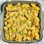 A square baking dish filled with sourdough stuffing mixed with chopped onions, celery, and herbs, set on a striped cloth.