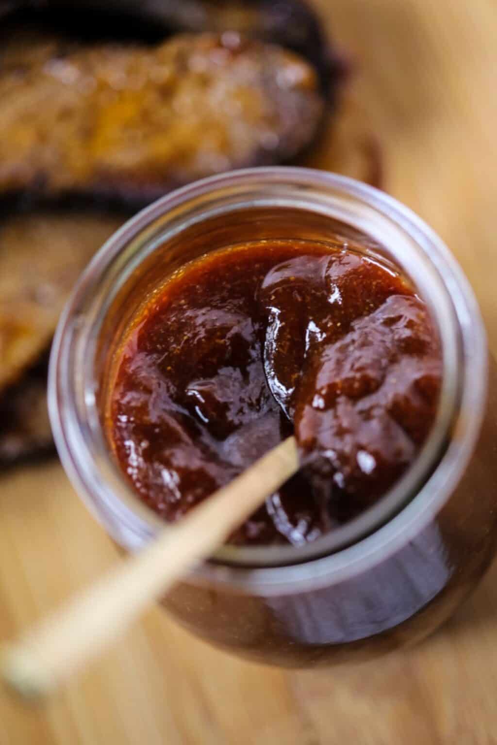 A jar of the sweet and spicy bbq sauce with a spoon inside.