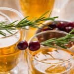 Three glasses of the drink garnished with fresh rosemary sprigs and cranberries, are arranged on a light-colored surface.