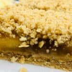 Close-up of apple oatmeal bars with a visible fruit filling layer and a crumbly, golden-brown topping on a parchment-lined surface.