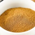 A white bowl filled with a mound of finely ground Apple Pie Spice, placed on a wooden surface.