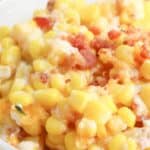 A bowl of rich corn casserole with cream cheese, topped with crispy bacon bits.