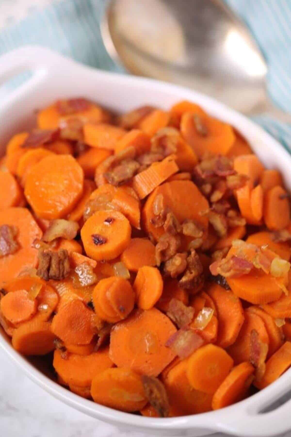 A white dish filled with brown sugar carrots and pecans creates a delightful harmony of flavors. A silver spoon rests in the background, ready to serve.
