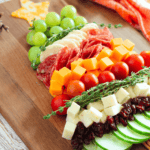 A cutting board with vegetables, meats and cheeses.