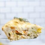 A close-up of a slice of savory Easy Turkey Pot Pie, filled with vegetables and what appears to be chicken or turkey, held up against a white tiled background.