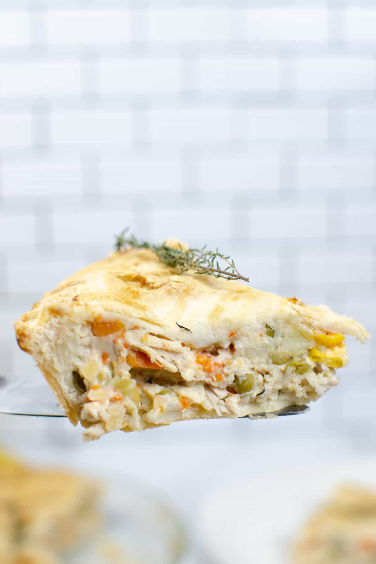 A close-up of a slice of savory Easy Turkey Pot Pie, filled with vegetables and what appears to be chicken or turkey, held up against a white tiled background.