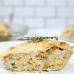 A slice of easy turkey pot pie with a golden crust, filled with tender turkey, mixed vegetables, and creamy sauce, garnished with a sprig of thyme on a white plate.