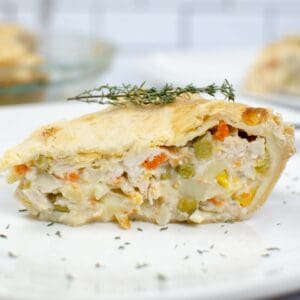 A slice of Easy Turkey Pot Pie with a golden crust, filled with tender vegetables and turkey, garnished with a sprig of thyme on a white plate.