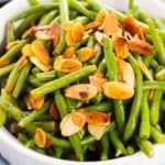 A white bowl filled with Green Beans and Almonds, featuring cooked green beans topped with toasted almond slices.