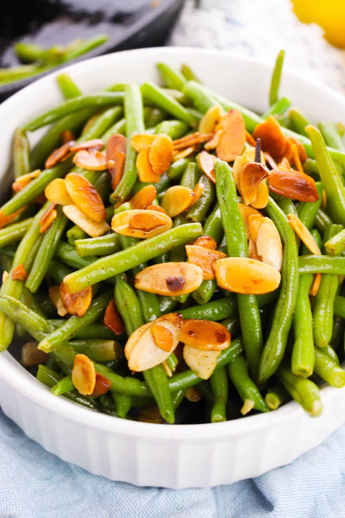 A white bowl filled with Green Beans and Almonds, featuring cooked green beans topped with toasted almond slices.