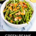 A white bowl filled with green beans and almonds, topped with toasted almond slices, sits elegantly on a light blue cloth.
