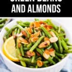 A white bowl filled with Green Beans and Almonds, topped with a lemon wedge, sits on a light blue cloth.