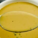 A close-up of a spoonful of creamy, light brown ham gravy held over a bowl filled with the same savory gravy.