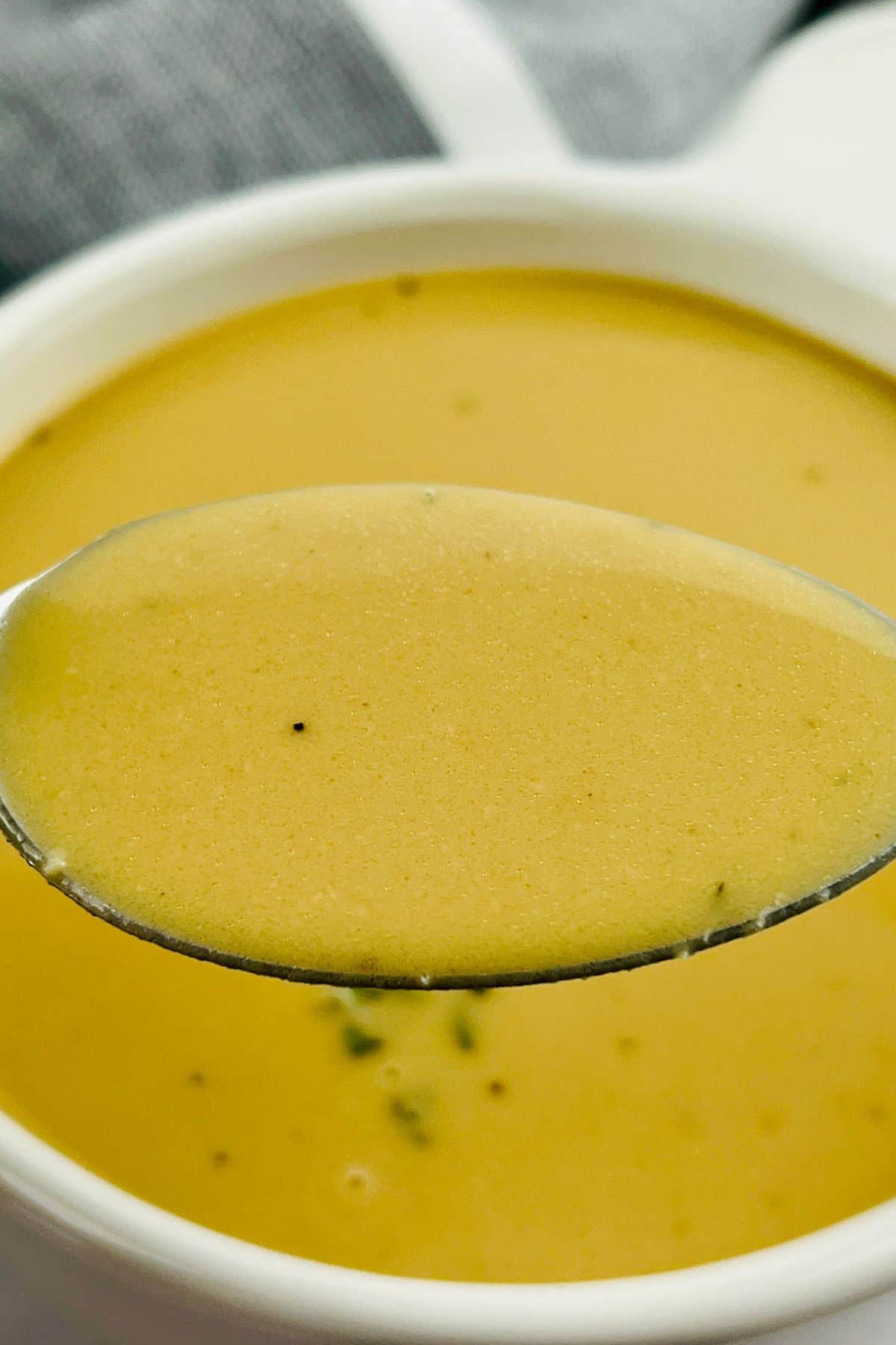 A close-up of a spoonful of creamy, light brown ham gravy held over a bowl filled with the same savory gravy.