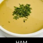 A bowl of rich Ham Gravy garnished with chopped herbs sits on a white surface, with the text "HAM GRAVY" displayed below.