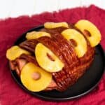 The meat on a black platter on a red table cloth.