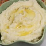 A bowl topped with melted butter and a sprinkle of black pepper, with a spoon and patterned cloth in the background.