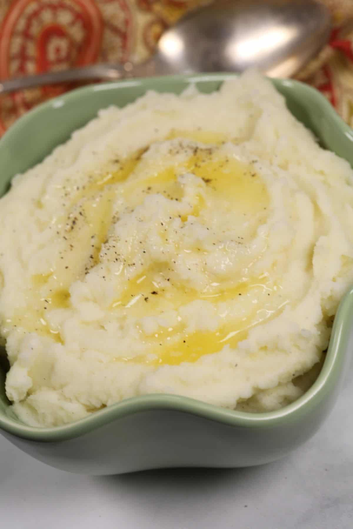 A bowl topped with melted butter and a sprinkle of black pepper, with a spoon and patterned cloth in the background.