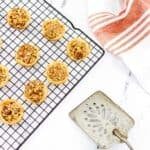 Freshly baked pecan tarts cool on a black wire rack, accompanied by a vintage metal spatula and a white and red striped towel, all set atop a smooth marble surface.