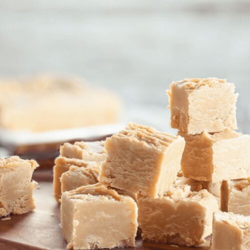 A stack of pieces sits on a wooden board, with more fudge blurred in the background.