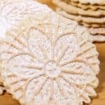 A close-up of round, treat dusted with powdered sugar, stacked on a wooden surface.