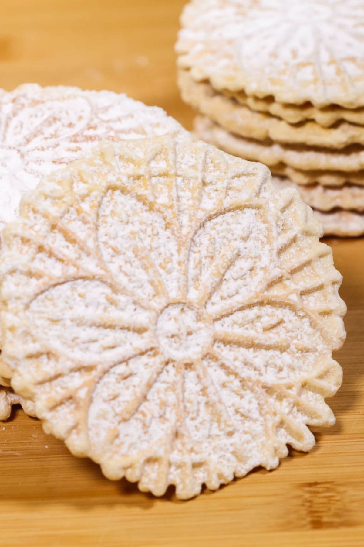 A close-up of round, treat dusted with powdered sugar, stacked on a wooden surface.