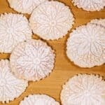 Pizzelle cookies with intricate floral patterns, dusted with powdered sugar, are beautifully arranged on a wooden surface.