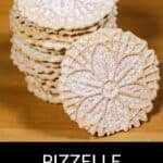 A stack of classic Pizzelle Cookies dusted with powdered sugar sits on a wooden surface, with one cookie propped in front. The text below reads "Pizzelle Cookies.