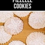 Round pizzelle cookies dusted with powdered sugar are arranged on a wooden surface, beneath a sign that reads "Crispy Pizzelle Cookies," highlighting the classic charm of these traditional Italian pizzelle cookies.