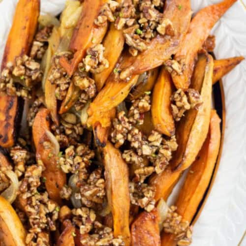 A plate of roasted spicy sweet potato wedges topped with chopped candied walnuts and caramelized onions.
