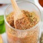 A glass jar filled with a mixed seasoning blend, labeled Smoked Turkey Dry Rub, with a wooden spoon resting inside.