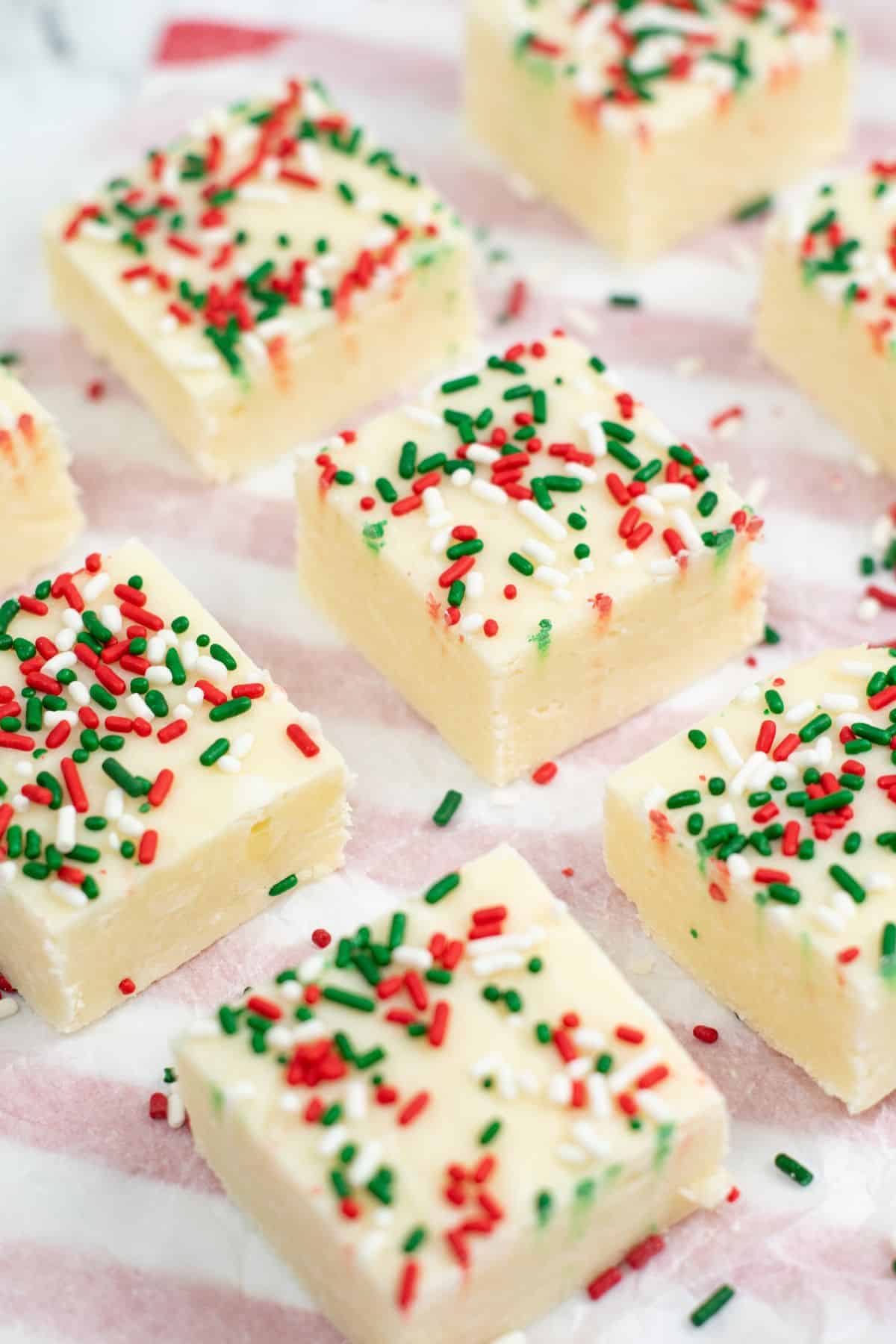Squares topped with red, green, and white sprinkles are arranged on striped parchment paper.