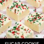 Squares of sugar cookie fudge with festive red and green sprinkles arranged on parchment paper. Text at the bottom reads "SUGAR COOKIE FUDGE.