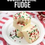 Squares of Sugar Cookie Fudge with red and green sprinkles are stacked on a white plate, set on a red and white striped cloth.