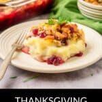 A serving of Thanksgiving Leftovers Casserole with stuffing, mashed potatoes, and cranberry sauce sits on a plate, with a fork and the casserole dish in the background.