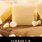 Squares of vanilla fudge stacked on a wooden surface, surrounded by white chocolate chips. The text "VANILLA FUDGE" is displayed at the bottom, perfect for inspiring your next homemade Vanilla Fudge Recipe.