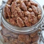 A glass jar filled with nuts, their sugar-coated surfaces glistening, shown in close-up on a light background.