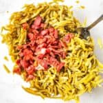 A glass bowl filled with Green Beans with Bacon and Onion, featuring chopped cooked bacon and vibrant green beans, with a metal spoon resting inside.