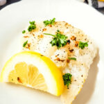 A white plate with air fryer cod and lemon.
