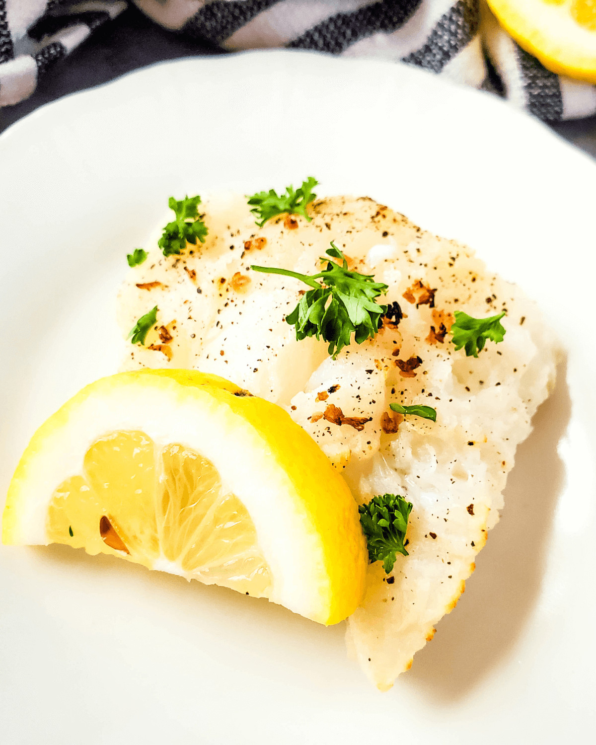 A white plate with air fryer cod and lemon.