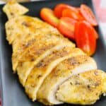 Baked Chicken Cutlets, sliced and seasoned, served on a black plate with halved cherry tomatoes.