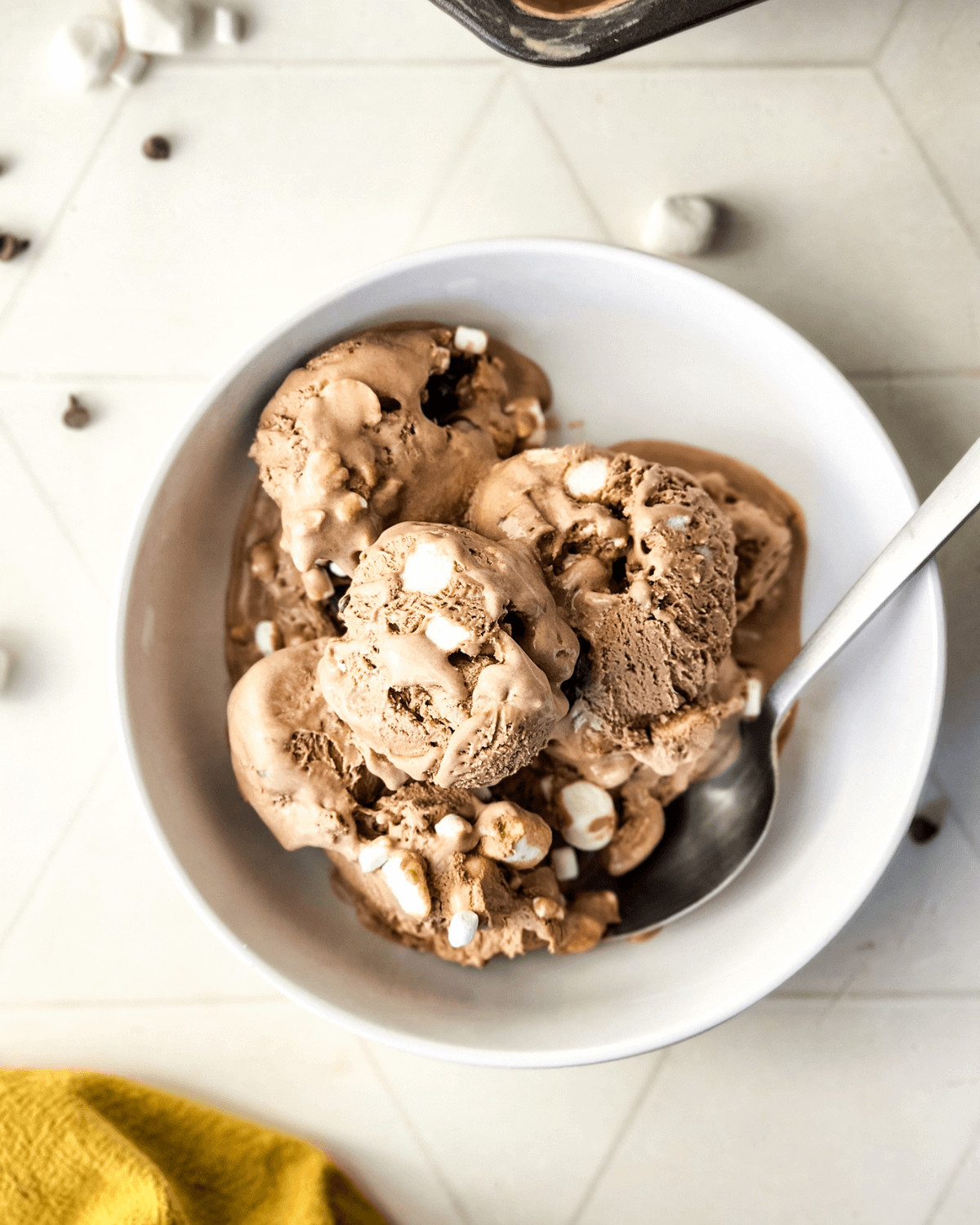 A bowl of cocoa condensed milk ice cream with marshmallows, chocolate chips, and condensed milk.