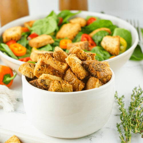 A bowl of homemade croutons atop a bed of fresh salad.