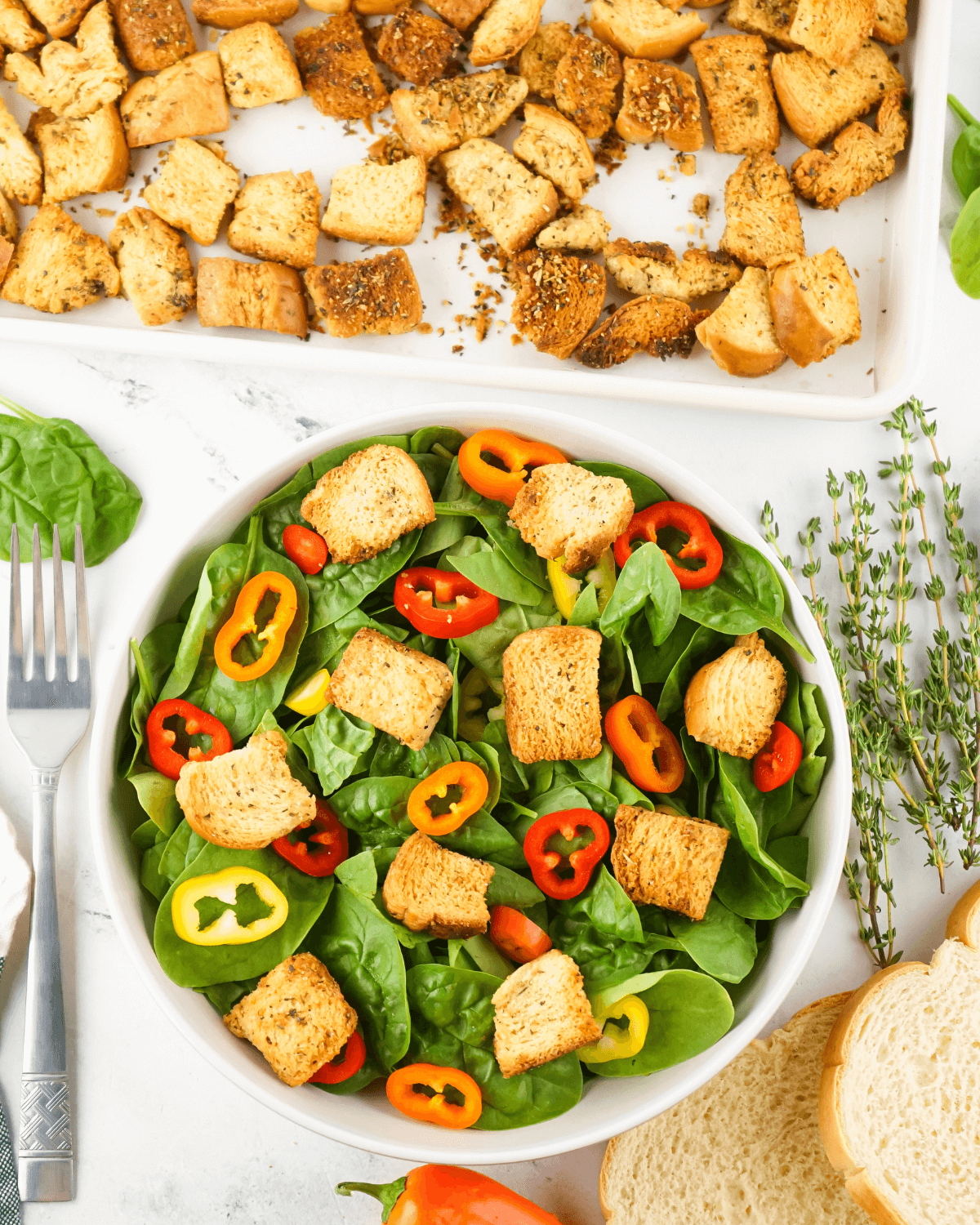 A bowl of spinach salad with homemade croutons and peppers.