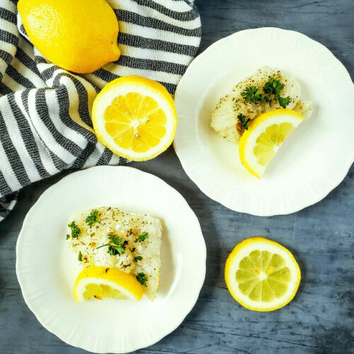 Two plates of fish with lemon slices on a table.