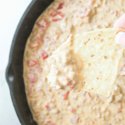 A person is dipping a tortilla into a bowl of dip.
