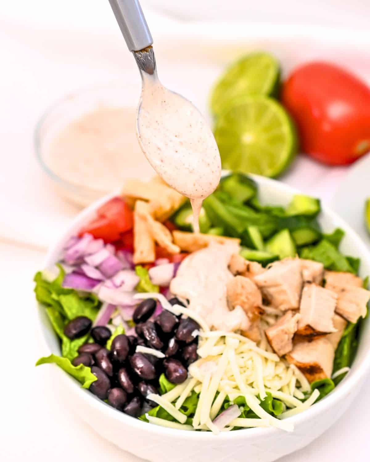 A white bowl filled with spicy southwest salad and dressing drizzled on it. 
