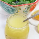 A jar of citrus vinaigrette next to a bowl of spinach and blueberries.